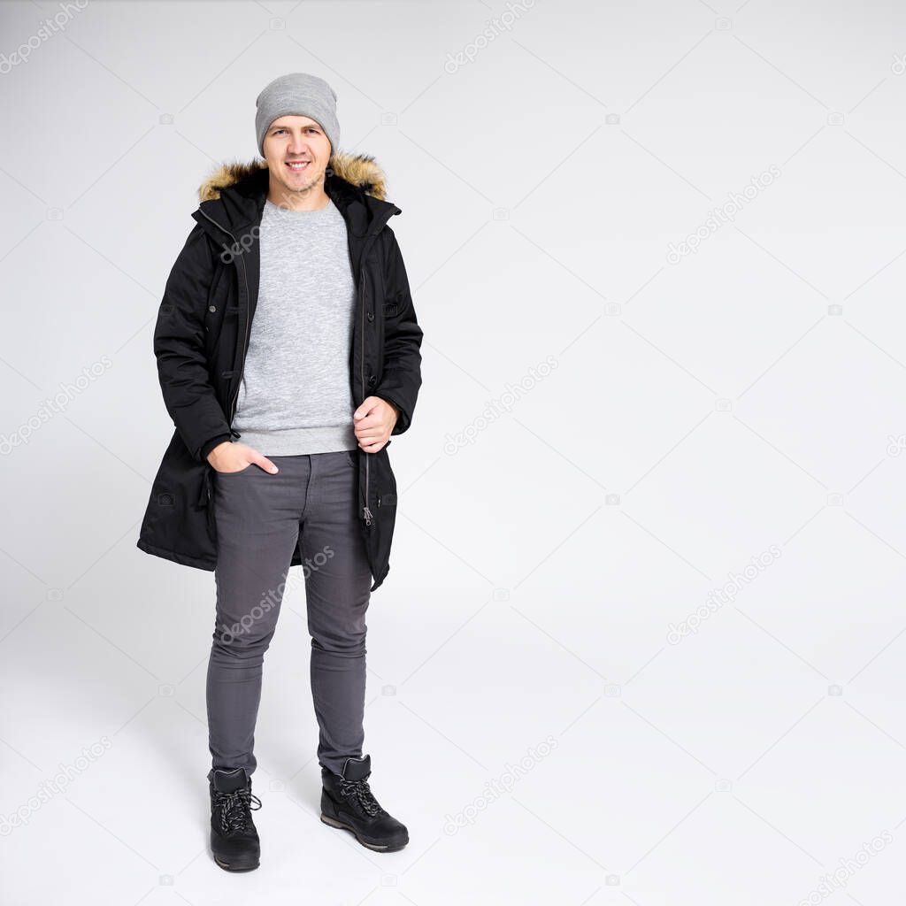 fell length portrait of young handsome man posing in warm winter clothes over gray background with copy space