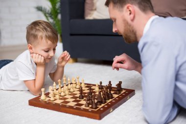 Küçük baba ve oğlu evde yerde yatıp satranç oynuyorlar.