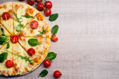 Domatesli ve otlu dilimlenmiş pizzanın üst görüntüsü ahşap masa zemininde fotokopi alanı ile