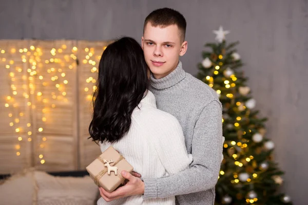 クリスマス 愛と驚きのコンセプト ハンサムな男はクリスマスツリーの背景にクリスマスプレゼントで彼のガールフレンドを驚かせます — ストック写真