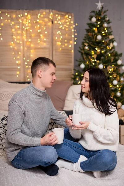 クリスマス 新年と愛のコンセプト かわいいカップルがクリスマスツリーの近くでお茶やコーヒーを飲む — ストック写真