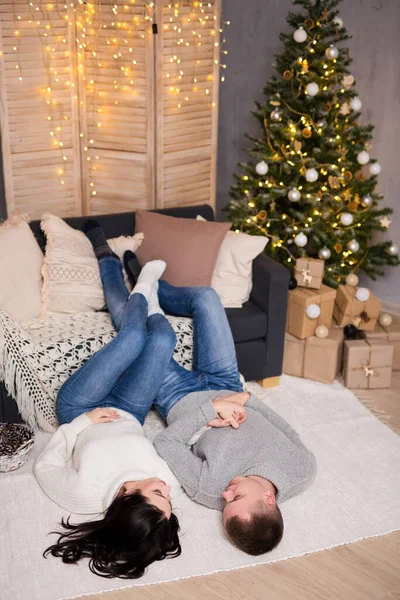 クリスマス 愛のコンセプト クリスマスツリーとギフトボックス付きの装飾されたリビングルームでリラックスした愛の若いカップル — ストック写真