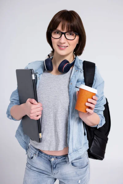 Uśmiechnięta Kobieta Szelkami Zębach Laptopie Filiżance Kawy Plecaku Szarym Tle — Zdjęcie stockowe