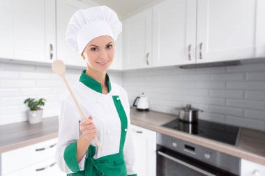 Modern mutfakta ahşap kaşıkla aşçı üniforması içinde genç ve mutlu bir kadın.