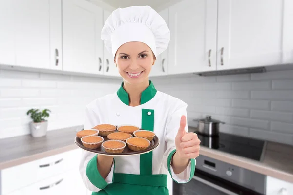 在现代厨房里 身穿制服的年轻漂亮的厨师女人拿着盘子 上面有松饼和大拇指 — 图库照片