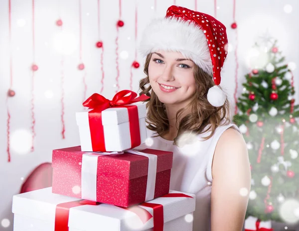 サンタの帽子の若い女性の肖像飾りクリスマスツリーの近くのプレゼントのヒープと — ストック写真