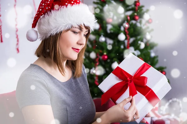 サンタ ハットの幸せな若い女性装飾されたクリスマスツリーの近くにギフトボックスを開く — ストック写真