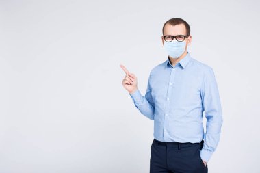 Coronavirus, salgın hastalık, karantina ve sağlık konsepti - tıbbi koruyucu maskeli genç işadamının portresi gri arka plandaki bir şeyi işaret ediyor