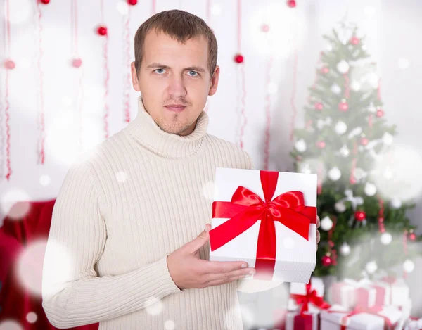 装飾されたリビングルームでクリスマスプレゼントボックスを持っている若い男 — ストック写真