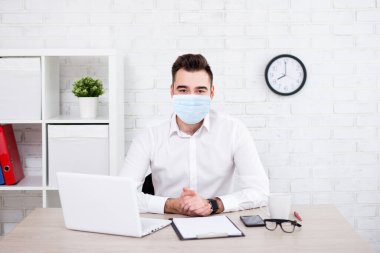 Coronavirus, salgın hastalık, karantina, sağlık ve ofis işi konsepti - koruyucu sağlık maskeli yakışıklı iş adamı ofiste oturuyor veya evde çalışıyor