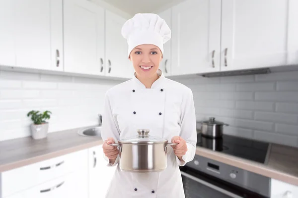 穿着厨师制服的年轻漂亮的女人拿着平底锅在现代的白色厨房里 — 图库照片