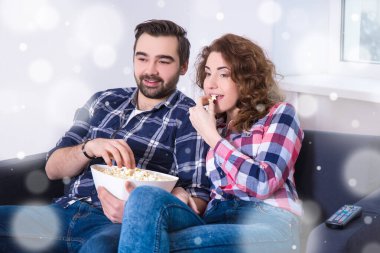 Kış tatili konsepti. Evde patlamış mısırlı genç bir çift televizyonda film izliyor.