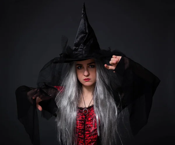 woman in black witch halloween costume and hat posing over black background