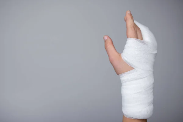 injury and first aid concept - male hand wrapped in bandage and gypsum over gray background with copy space