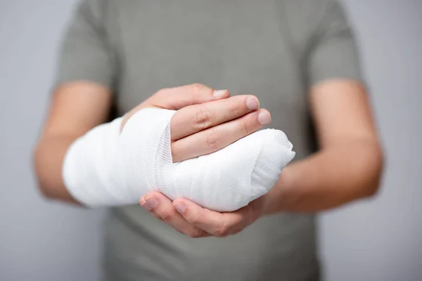 first aid concept - close up of broken male hand with bandage and gypsum