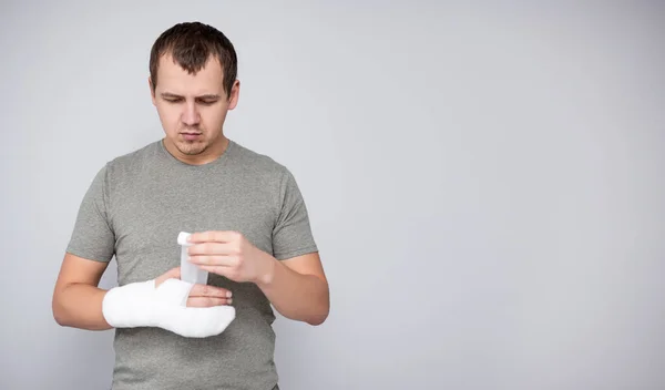 fracture and first aid concept - young man bandaging his hand after accident and copy space over gray wall background