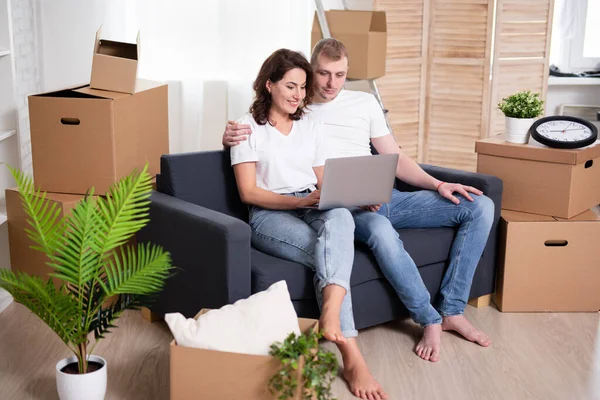 happy young couple using laptop surrounded by cardboard boxes ready to moving day