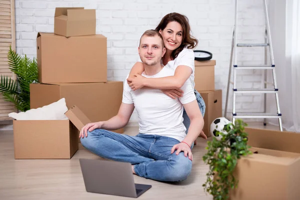 moving day - portrait of young couple using laptop in new apartments surrounded with cardboard boxes