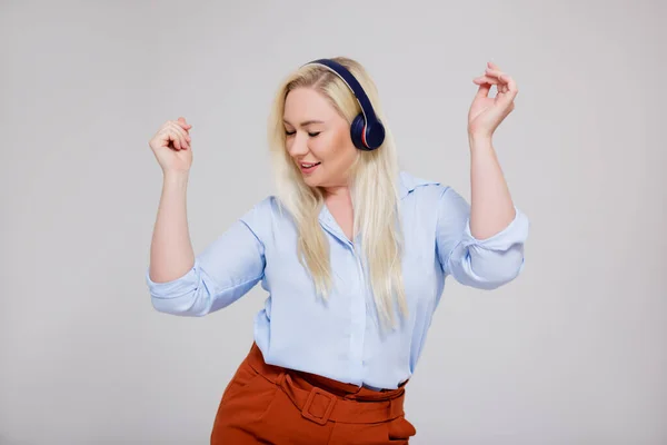 portrait of beautiful plus size blonde woman listening music and dancing over gray background