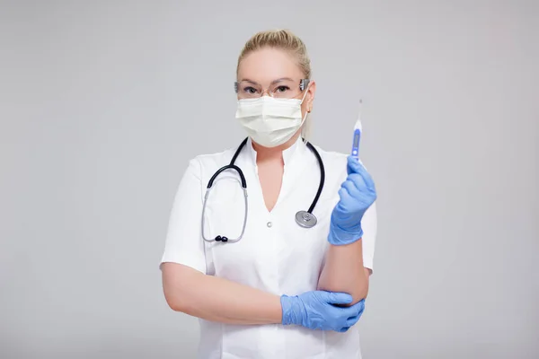 ヘルスケアとコロナウイルスパンデミックの概念 コピースペースで灰色の背景に温度計を保持白い制服と保護マスクの女性医師または看護師 — ストック写真