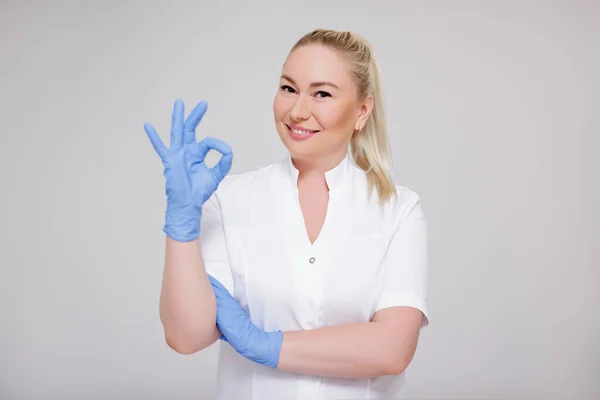 保健和美容学概念 穿着白色制服和蓝色手套的女医生 护士或美容师的肖像 在灰色背景上有清晰的标志 有复制空间 — 图库照片