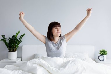 Evde ya da otelde uyandıktan sonra yatakta gerinen genç kadının portresi.