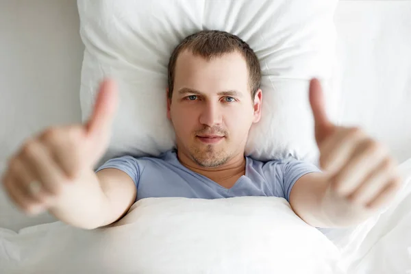 Genç Yakışıklı Bir Adamın Yatakta Yatıp Başparmağını Kaldırmasının Iyi Görüntüsü — Stok fotoğraf