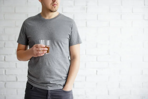 アルコール依存症の概念 コピースペースと白いレンガの壁の背景にウイスキーのガラスを保持若い男 — ストック写真