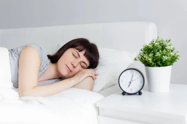 自宅のベッドで寝ている美しい女性の肖像ベッドサイドテーブルの目覚まし時計 — ストック写真