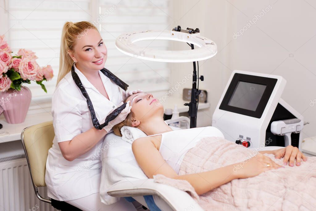 make up and beauty concept - attractive beautician applying permanent make up on eyebrows at modern beauty salon