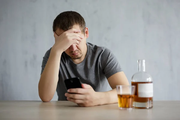 アルコール依存症 うつ病の概念 若いストレスのある男を使用してスマートフォンや自宅やパブでウイスキーを飲む — ストック写真