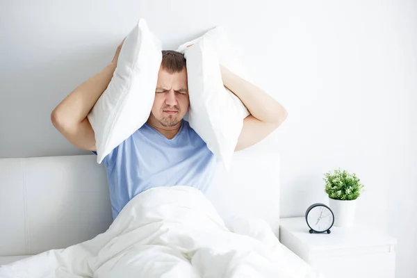うつ病不眠症と頭痛の概念 ベッドに座って枕を頭の上に持っている疲れた青年の肖像画 — ストック写真