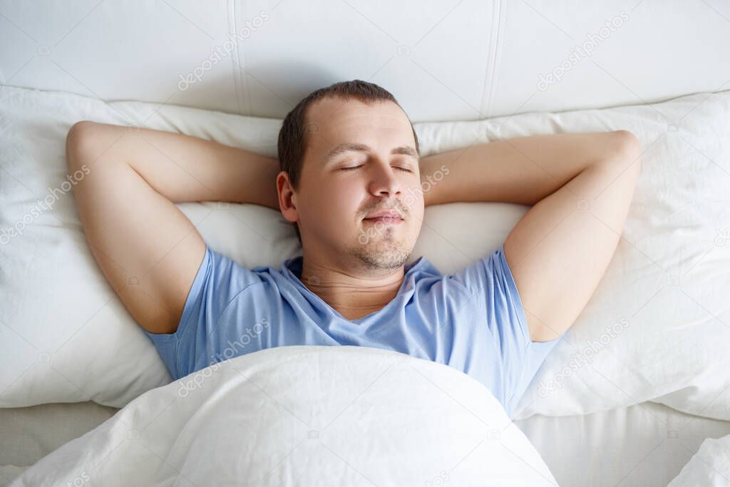 relaxation and healthy lifestyle concept - top view of young handsome man sleeping in bed