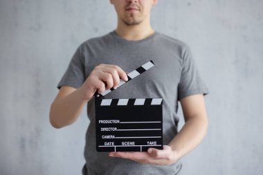 Video ve film yapımcılığı konsepti. Gri arka plan üzerinde elinde alkış tahtası tutan genç bir adam.