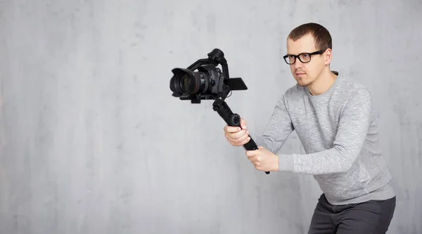 3軸ジンバル上の現代のDslrカメラを使用してプロのビデオカメラマン撮影ビデオの肖像画コピースペースとグレーのコンクリート壁の背景 — ストック写真