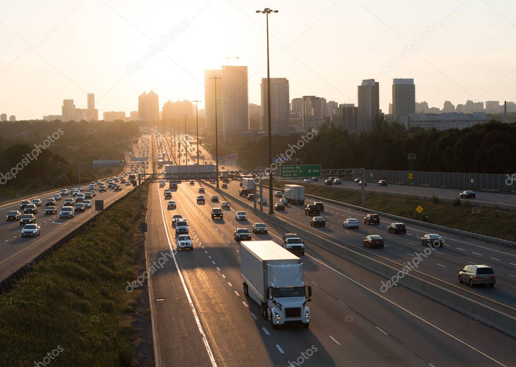 View of busy Highway 401 in Toronto Canada with reflection and high rise buildings during rush hours at the sunset