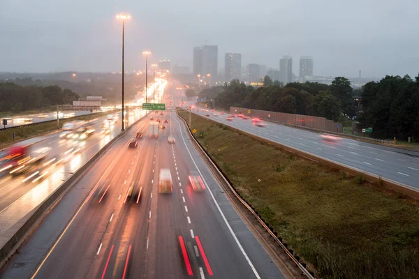 View of highway 401 in Toronto on drizzle rain with trail lights and high rise buildings at sunset