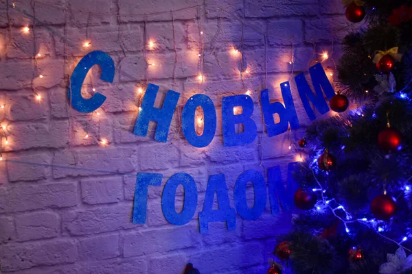 Frohes neues Jahr auf Russisch auf Backsteinhintergrund neben einem Weihnachtsbaum, der mit einem Kranz beleuchtet ist — Stockfoto