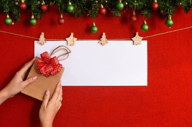 Bir yazı ve yılbaşı hediyesi için bir çarşaf. Kırmızı arka planda Noel ağacı dalları olan bir hediye.
