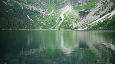 Kristal berrak suya sahip dağ gölü yeşil yamaçları ve kayalık tepeleri yansıtarak el değmemiş vahşi doğada doğal bir manzara yaratır. Dağ gölü suları tepeleri ve kayalıkları çevreleyen aynalar.,
