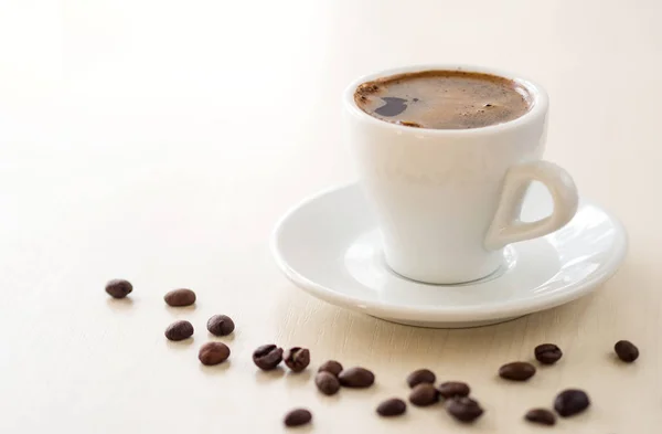 Πρωινό. Φλιτζάνι καφέ και κόκκους καφέ σε λευκό τραπέζι — Φωτογραφία Αρχείου
