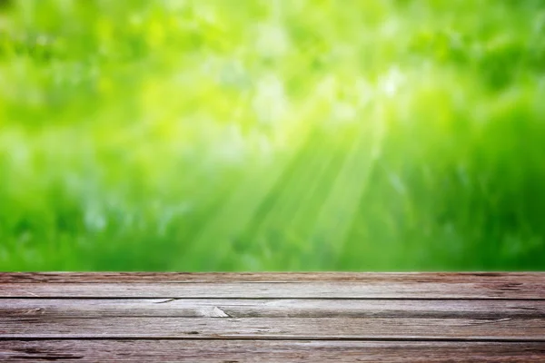 Meja kayu di latar belakang rumput hijau kabur dengan sinar matahari — Stok Foto