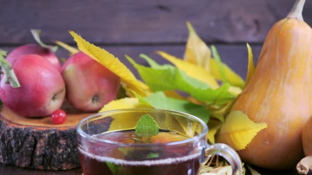 Té caliente sobre una mesa de madera sobre el fondo de la cosecha (calabazas, manzanas) y coloridas hojas otoñales . — Vídeos de Stock