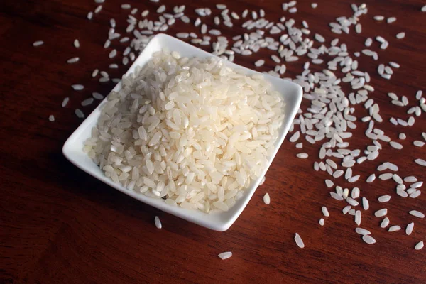 Taça branca com grãos de arroz branco em uma mesa de madeira, vista superior — Fotografia de Stock