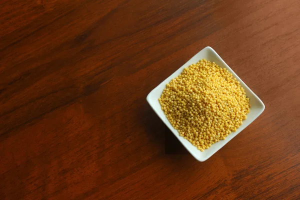 Tigela branca com grãos de milheto amarelo seco em uma mesa de madeira, vista superior . — Fotografia de Stock