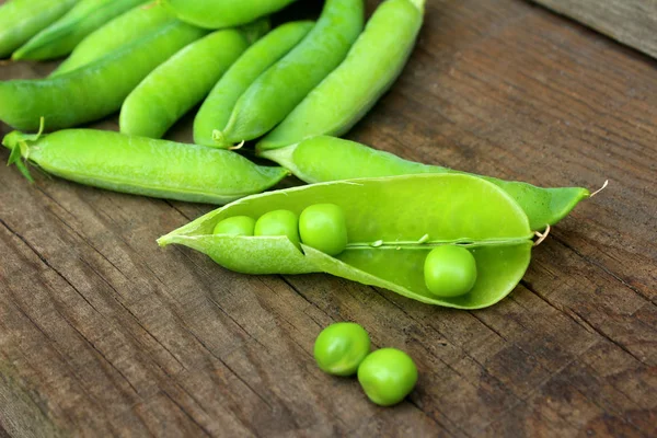 En hel del ärtor på trä bordet är stängda och öppna skida. Gröna mogna ärtor — Stockfoto