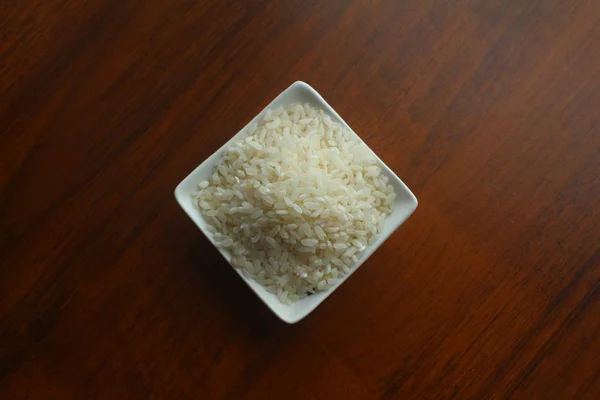 Cuenco blanco con granos de arroz blanco en una mesa de madera, vista superior . —  Fotos de Stock