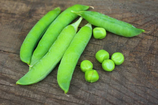 Vista de ervilhas verdes maduras frescas deitadas em uma mesa rústica. Ervilhas em uma vagem close-up — Fotografia de Stock