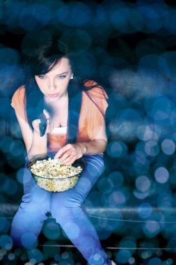 Genç bir kadın televizyon seyrediyor, patlamış mısır yiyor.