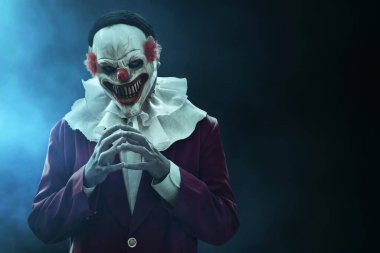 Karanlık arka planda, sis dumanlı korkunç palyaço maskesi takan adam, Cadılar Bayramı temalı.